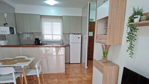 Eine kleine Küche mit Essbereich, weißen Schränken, einem Kühlschrank und einem Tisch mit Stühlen.
