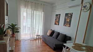 Ein Wohnzimmer mit einer Couch, einem kleinen Tisch, einer Topfpflanze und Kunstwerken an der Wand.