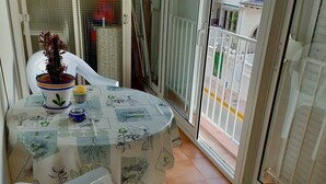 Ein Balkon mit Tisch, bedeckt mit einer Tischdecke mit Pflanzenmotiven, einer Topfpflanze und einem Plastikstuhl.