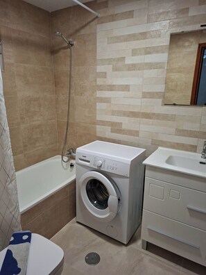 Ein kleines Badezimmer mit Waschmaschine, Badewanne und Waschbecken.