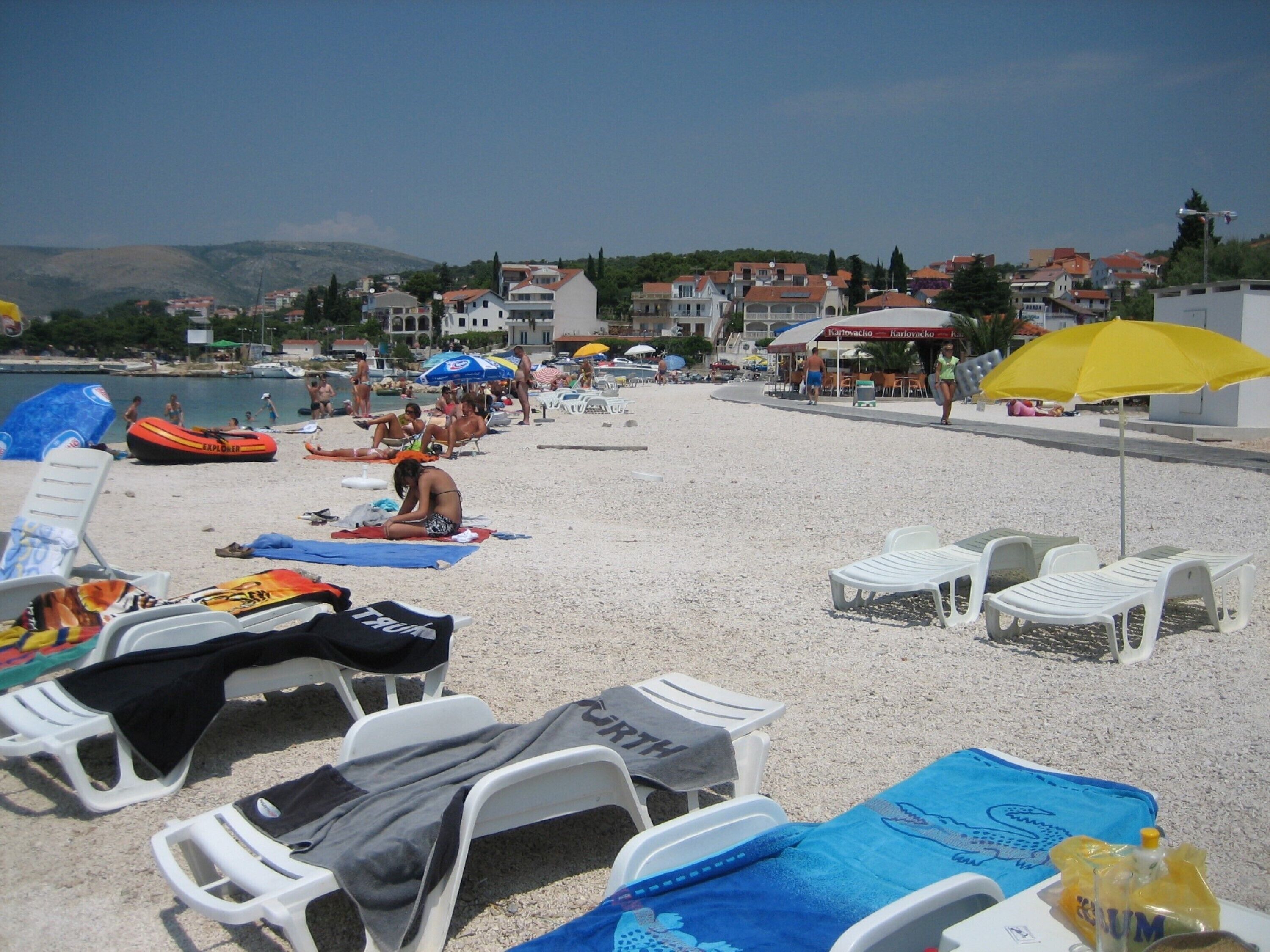 A beach with white lounge chairs, umbrellas, and a clear view of the sea and buildings in the background.