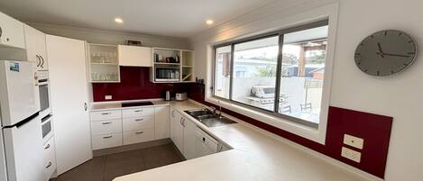 A compact kitchen with white cabinets, a red backsplash, a built-in oven, a sink, and a window with a view of the outside.