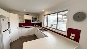 A compact kitchen with white cabinets, a red backsplash, a built-in oven, a sink, and a window with a view of the outside.