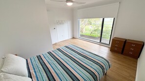 Une chambre à coucher comprenant un lit, une commode, un ventilateur de plafond et une fenêtre donnant sur un paysage verdoyant.
