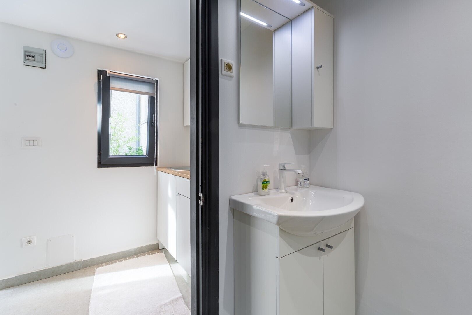 A modern bathroom with a white sink, a window, and a mirror above the sink.