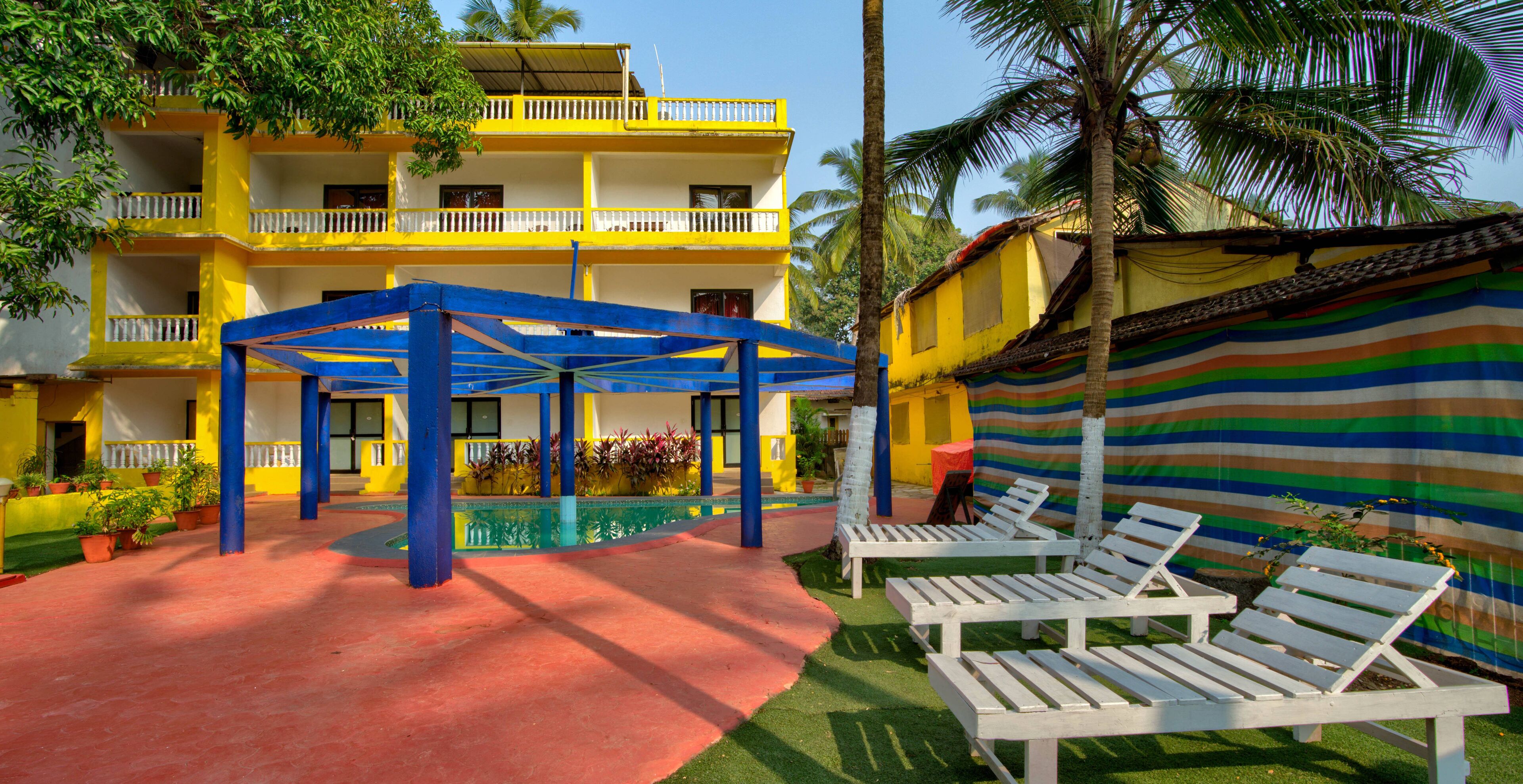 A multi-story yellow building with balconies, a covered seating area with white lounge chairs, and a striped awning.