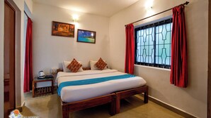 A hotel room with a bed, a nightstand, a window with curtains, and two paintings on the wall.