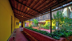 A covered corridor with a red floor, yellow walls, and a thatched roof.