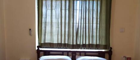 A hotel room with a bed, a nightstand, an air conditioning unit, and a window with green curtains.