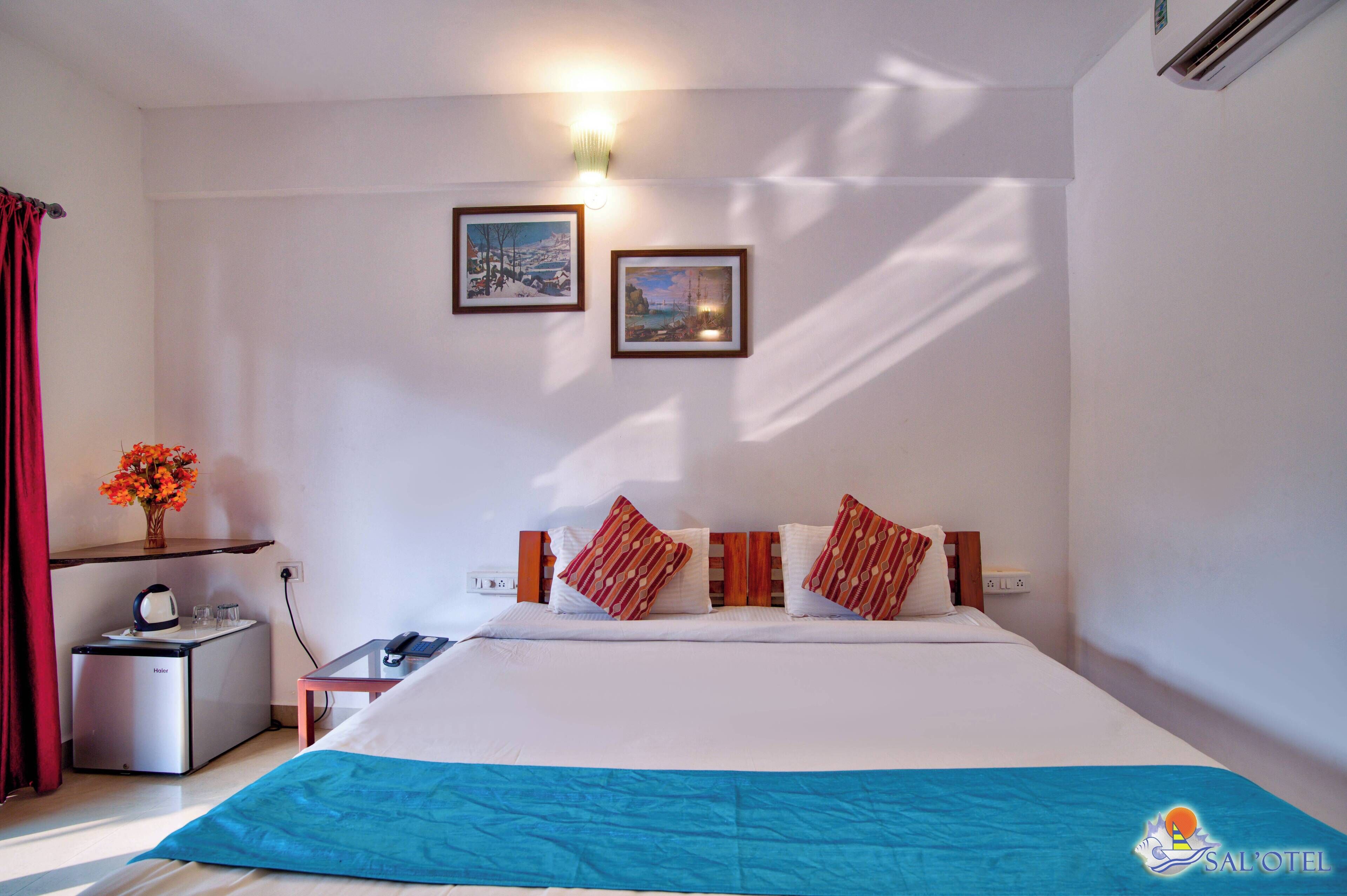Ein Hotelzimmer mit einem Bett, einem kleinen Tisch mit Wasserkocher, einer Vase mit Blumen und zwei gerahmten Bildern an der Wand.