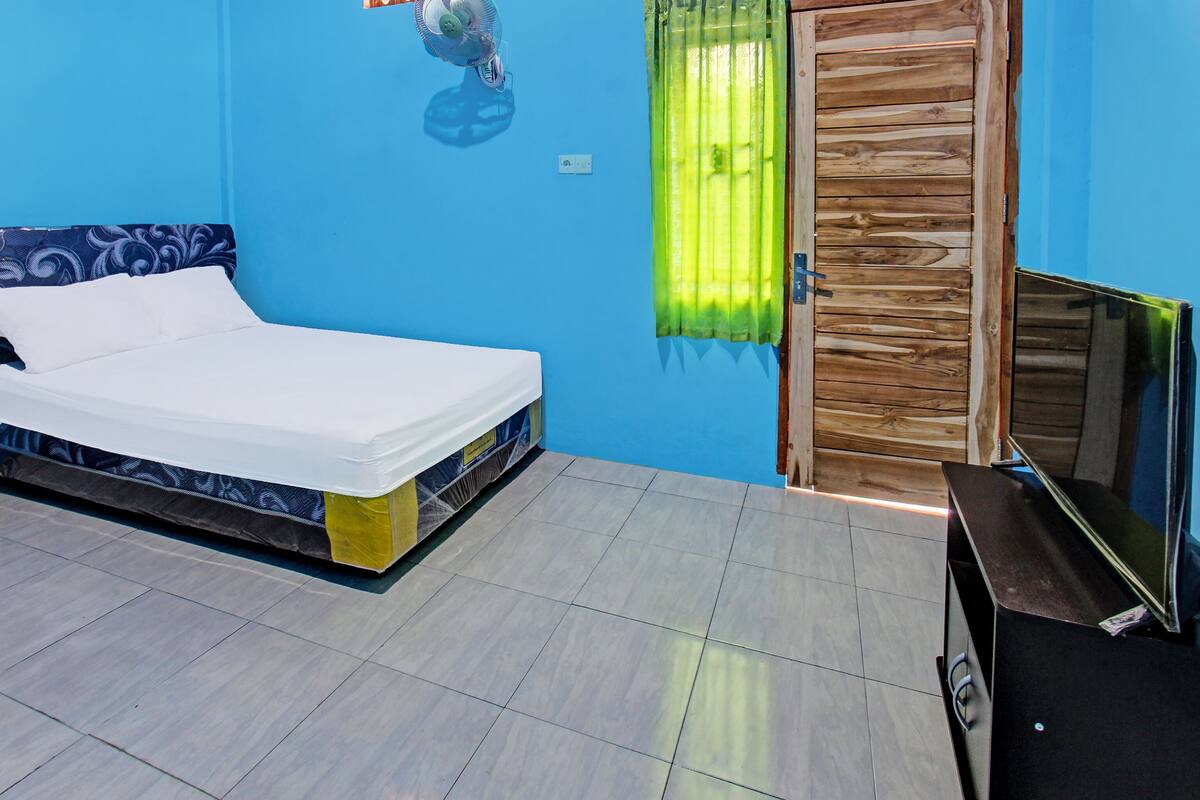 A room with a bed, a wooden door, a television, and a wall-mounted light fixture.