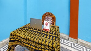 A room with a blue wall, a patterned tablecloth, a laptop, a decorative chair, and a poster on the wall. - SPOT ON 91811 Rumah Inap Bunda Nurhayati (Tanak Awu)