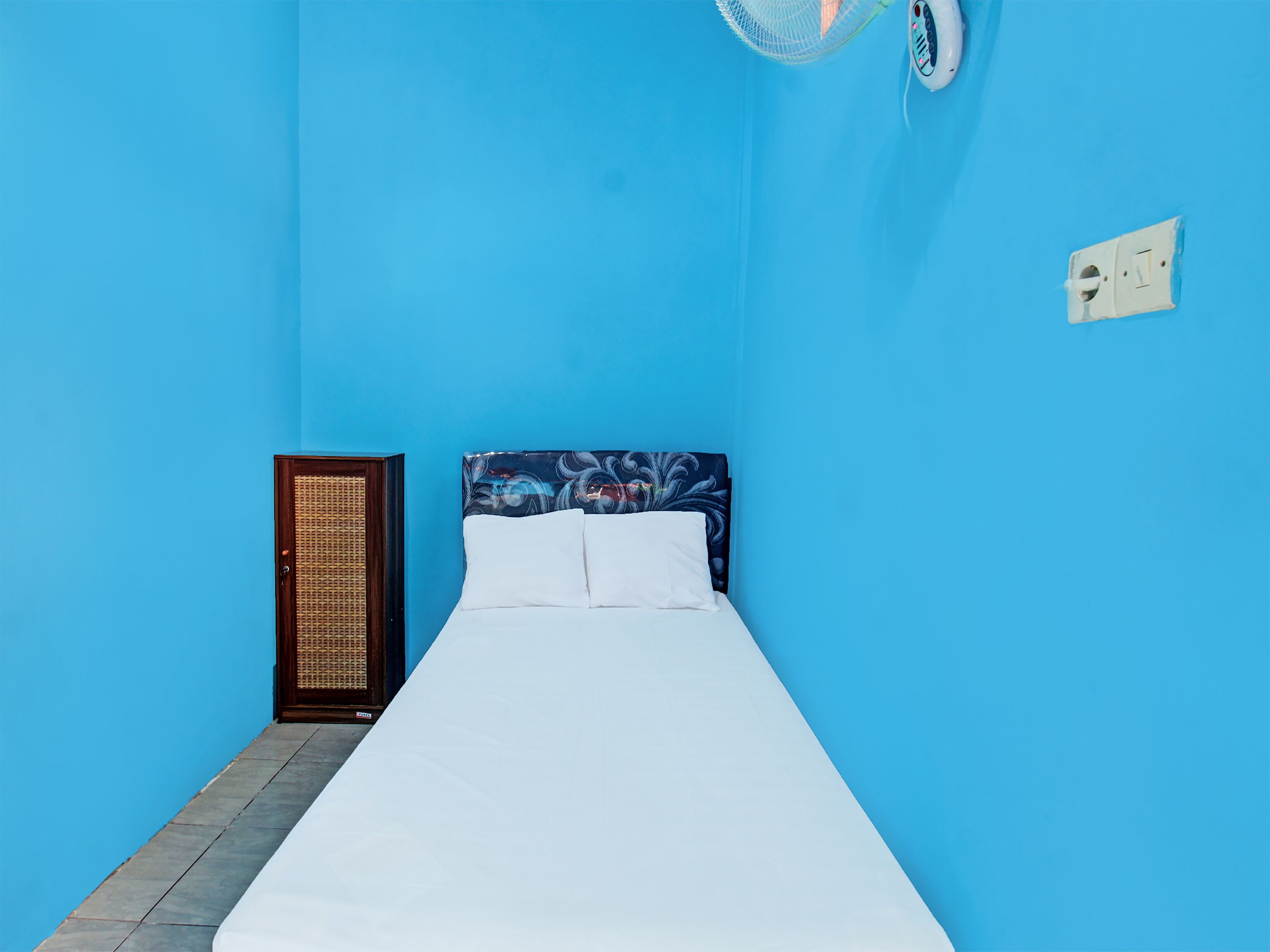 Una cama individual con ropa de cama blanca en una habitación con paredes azules.