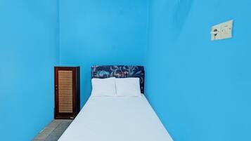 Una cama individual con ropa de cama blanca en una habitación con paredes azules.