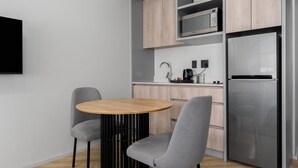 A modern kitchen with a round wooden table, two grey chairs, a stainless steel refrigerator, and wooden cabinets. - One Thibault 1628 (Cape Town)