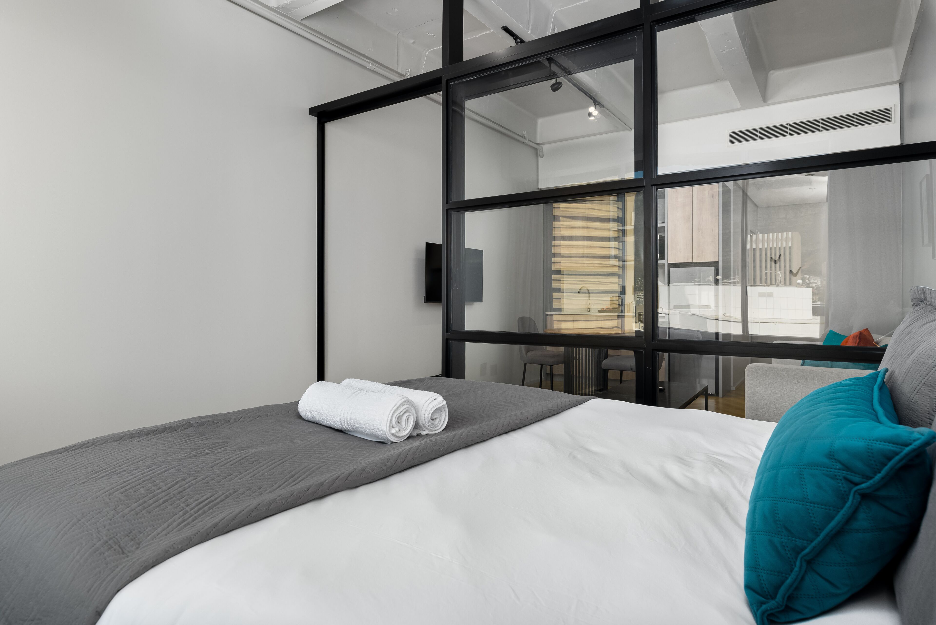 Ein modernes Hotelzimmer mit einem großen Bett, einer Glaskabine und Blick ins Badezimmer.