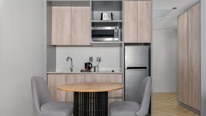 A modern kitchen with two grey chairs, a round wooden table, and built-in appliances including a microwave and refrigerator. - One Thibault 1628 (Cape Town)