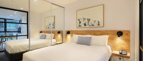 A hotel room with a large bed, a bedside table with a phone, and a mirror.
