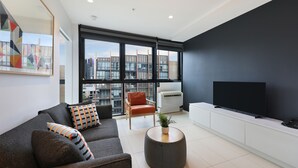 Un soggiorno moderno con un divano grigio, un tavolino rotondo, una televisione a schermo piatto e un'ampia finestra con vista sulla città.