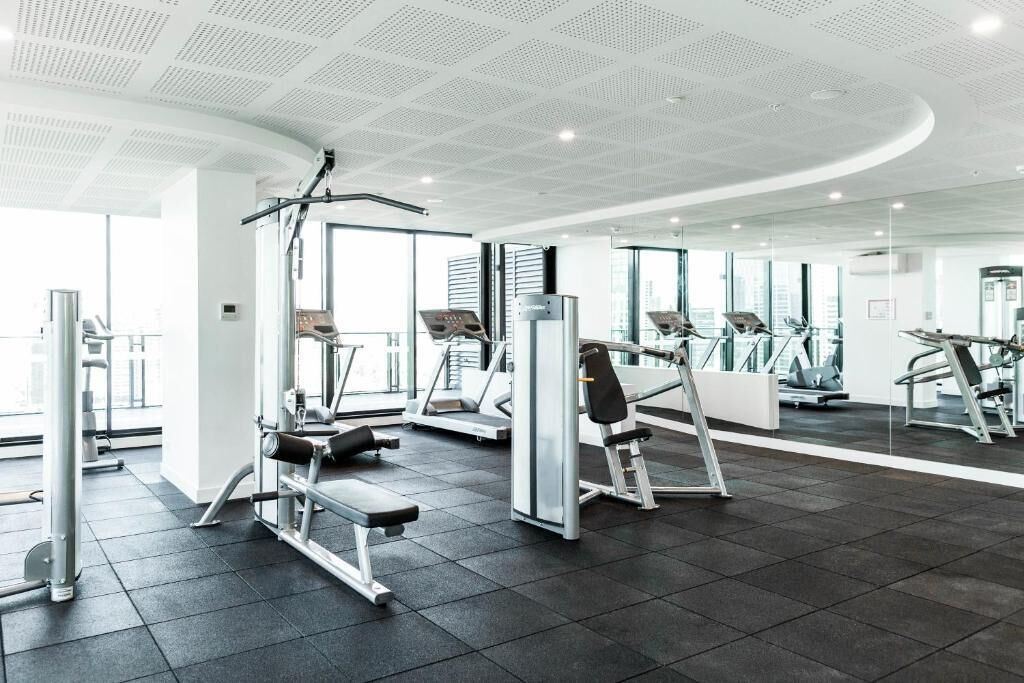 A modern gym with various exercise equipment, large windows, and a clean, spacious layout.