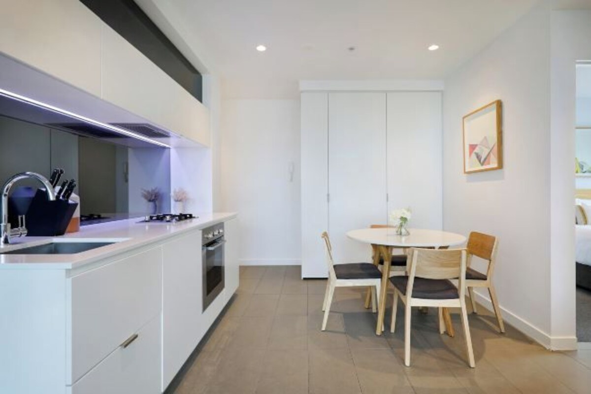A modern kitchen with white cabinetry, a gas stove, and a dining area with a round table and four chairs.