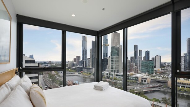 Camera d'albergo moderna con un letto grande, lenzuola bianche e vista sullo skyline cittadino tramite finestre a tutta altezza.