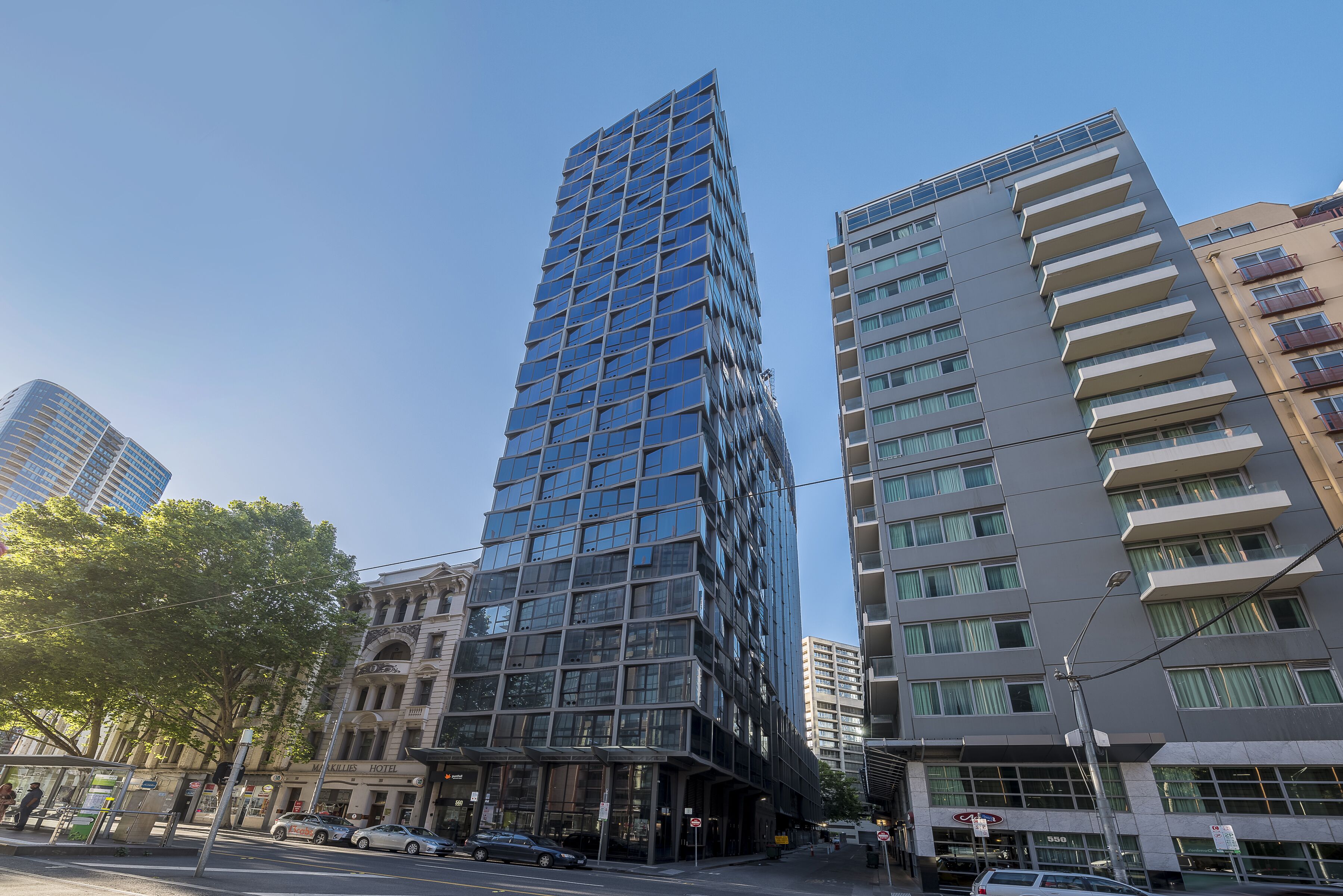 Een modern hoog gebouw met een glazen gevel, naast een lager gebouw met balkons.