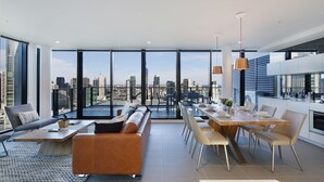 Un soggiorno moderno con vista sulla città, una zona pranzo con tavolo in legno e una cucina con mobili bianchi.