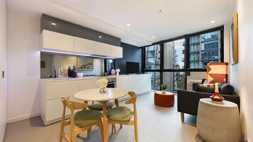 A modern kitchen with white cabinets, a dining area with a round table and chairs, and a living area with a sofa and a lamp.