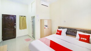 A hotel room with a bed, a wardrobe, a door, and an air conditioning unit.