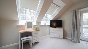 Quarto com claraboias, televisão, escrivaninha e cómoda.