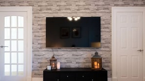 A room with a stone wall, a flat-screen TV mounted above a black console, and two lit lanterns on the console. - Mary Street Seaside Home in Stonehaven Aberdeenshire (Stonehaven)