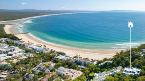 An aerial view of a coastal area with a beach, residential buildings, and a clear view of the ocean. - Panorama 4 Noosa Heads (Noosa Heads)