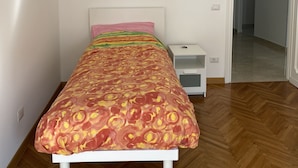 A bedroom with a bed, a nightstand, a white wall, a wooden floor, and a door leading to another room. - Spacious rooms in the center of Rome (Roma)
