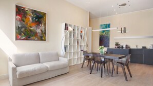 Ein modernes Wohnzimmer mit einer Couch, einem Esstisch mit Stühlen, einem Bücherregal und einer Küchenzeile.