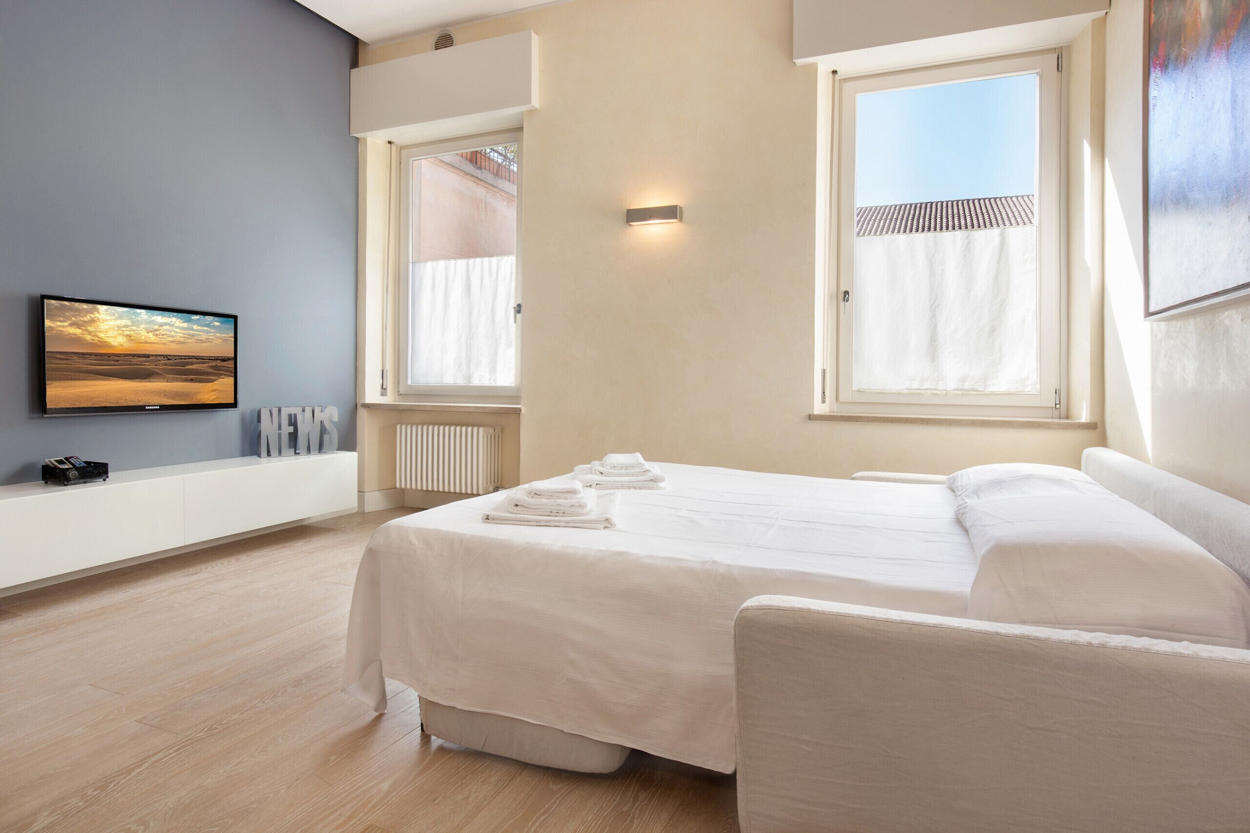 A modern hotel room with a large bed, a TV, and a view of the outside.