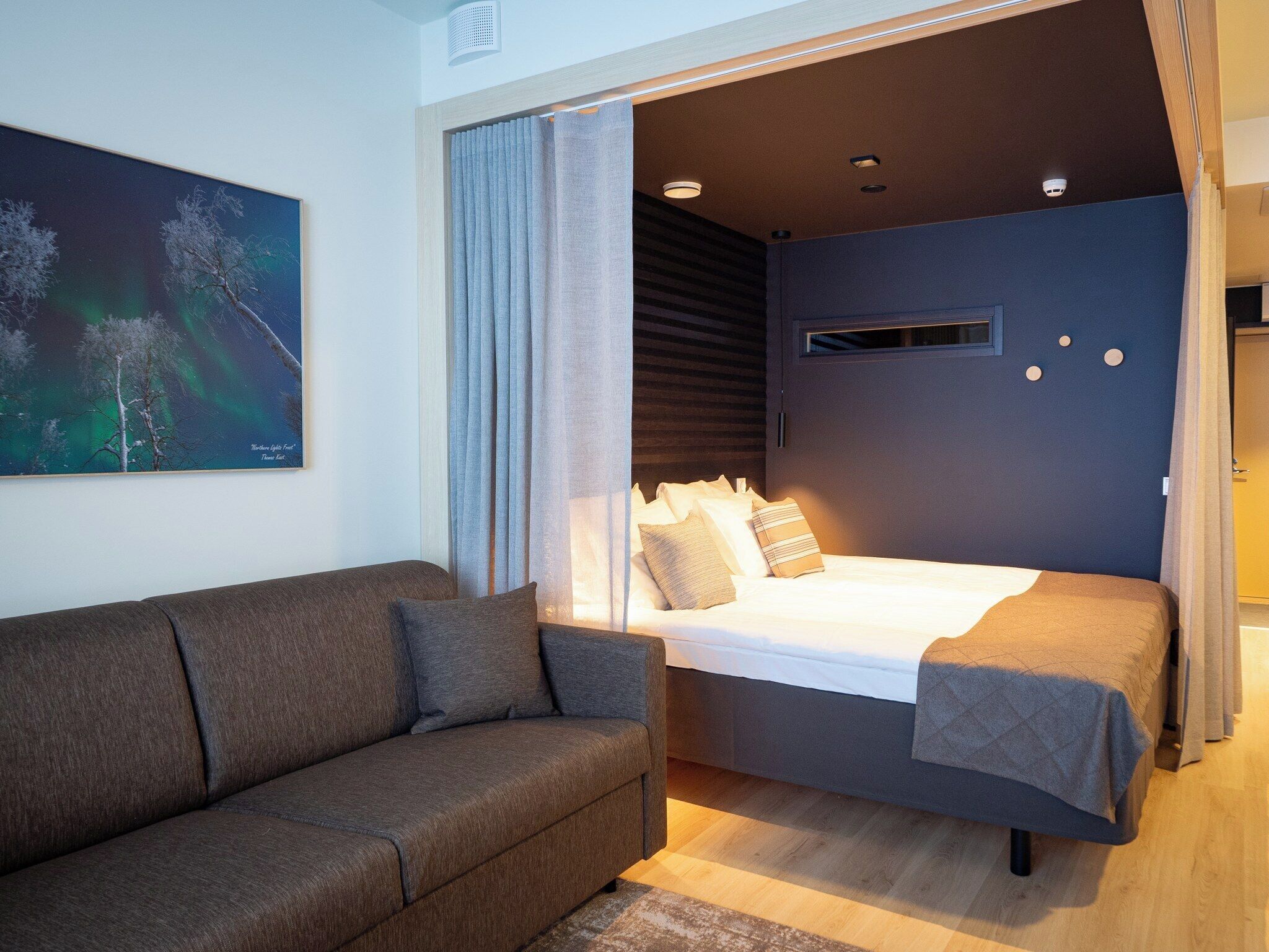Una habitación moderna con una cama, un sofá y un cuadro de auroras boreales.