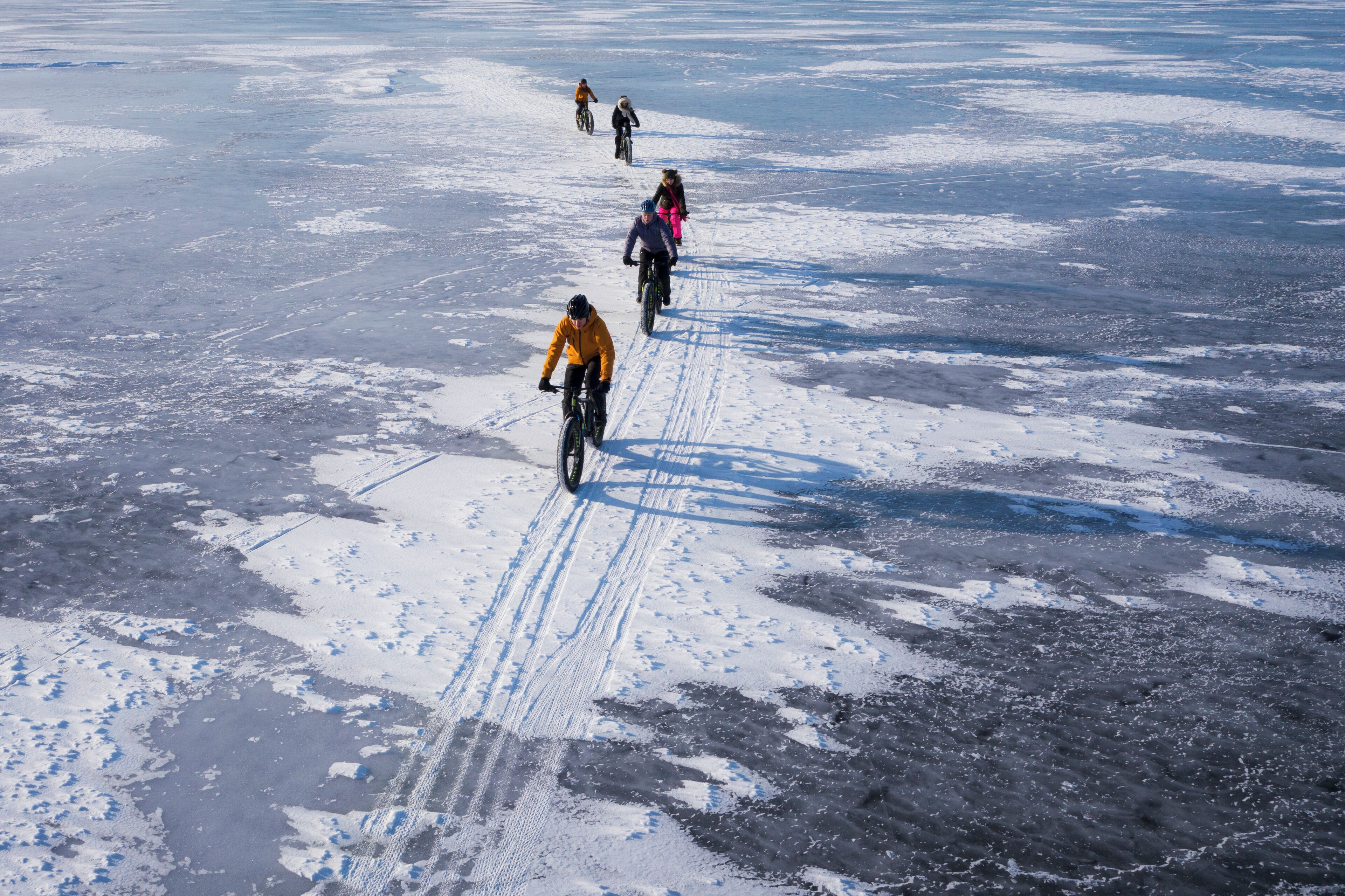 A group of people riding bicycles on a snowy surface.