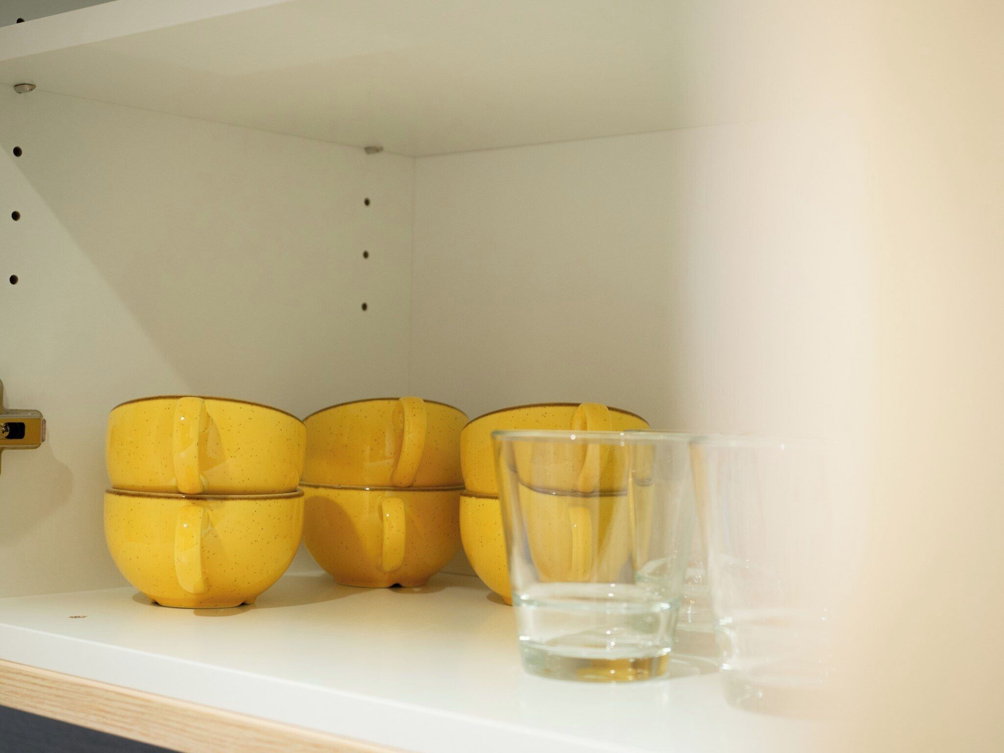 A shelf with three yellow ceramic mugs and a clear glass.