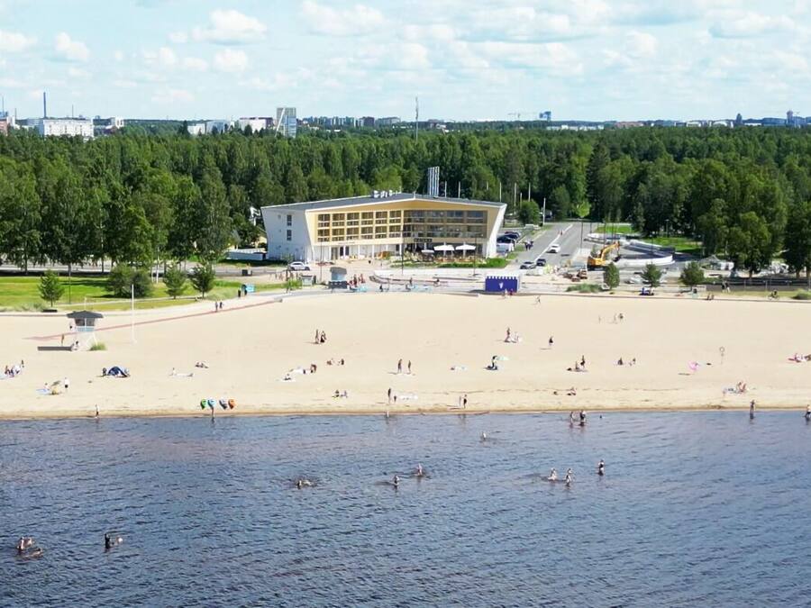 Une plage avec un grand bâtiment en arrière-plan, entourée d’arbres.