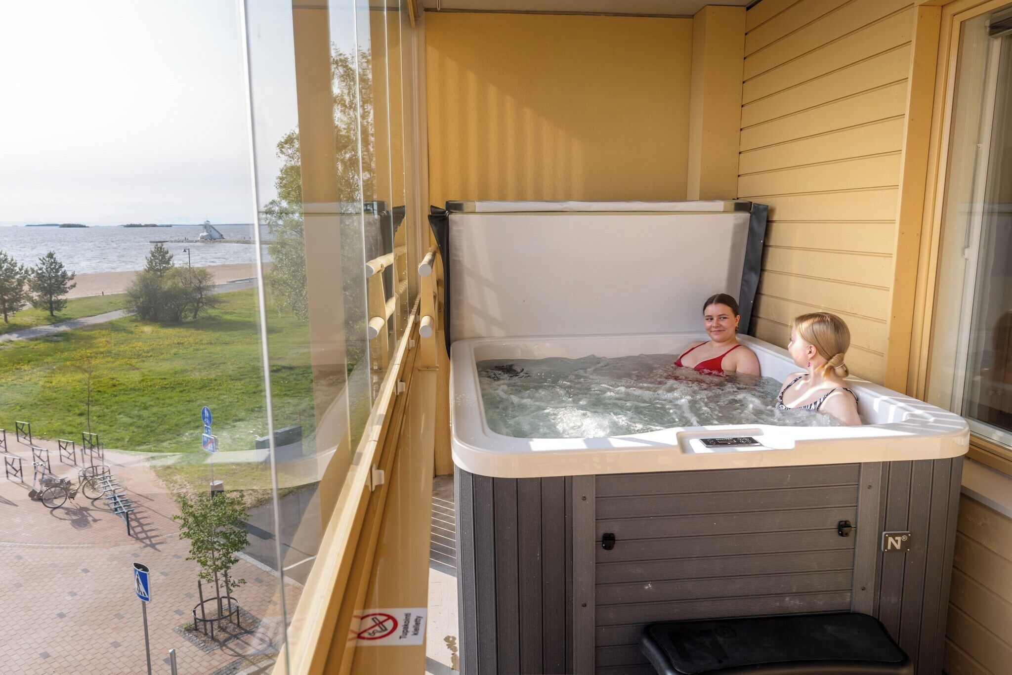 Un jacuzzi con dos personas en un balcón con vistas a la playa.
