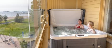 Un jacuzzi con dos personas en un balcón con vistas a la playa.