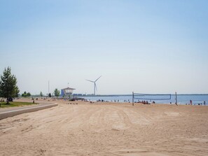 Uma praia arenosa com uma turbina eólica, uma torre salva-vidas e um céu claro.