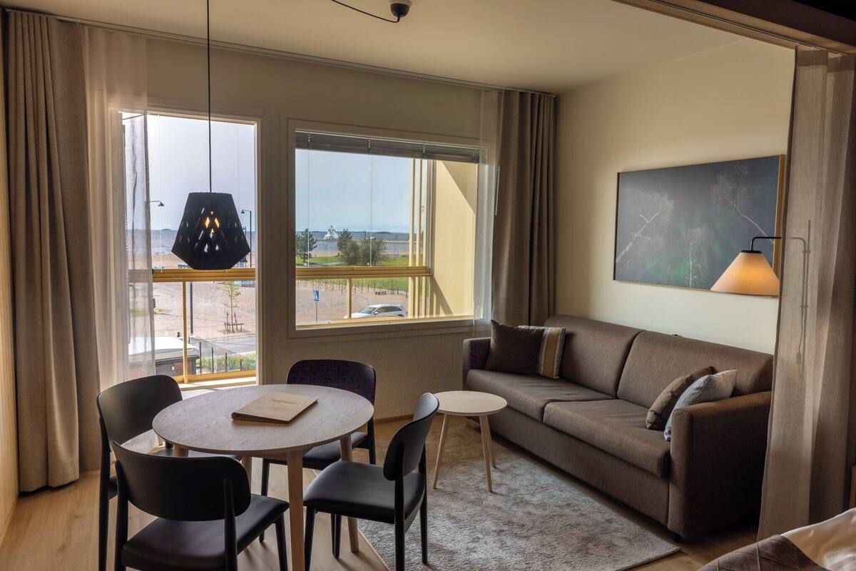 Ein Hotelzimmer mit einer Couch, einem kleinen Tisch, zwei Stühlen, einer Lampe und einem Gemälde an der Wand.