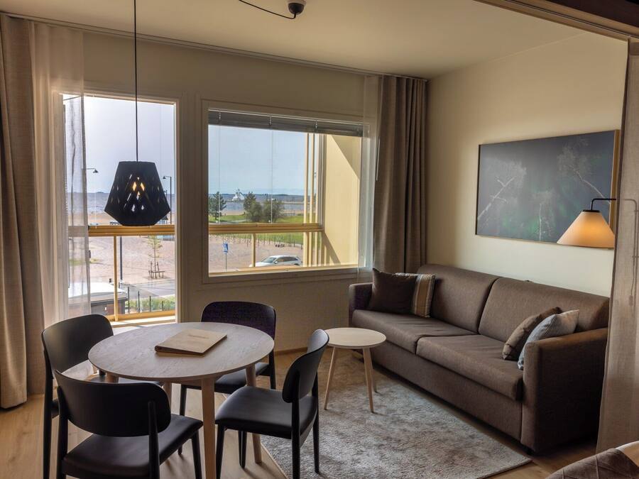A hotel room with a sofa, a small table, two chairs, a lamp, and a painting on the wall.
