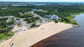 Vista aérea de una zona costera con playa arenosa, estacionamiento y una combinación de edificios residenciales y comerciales.