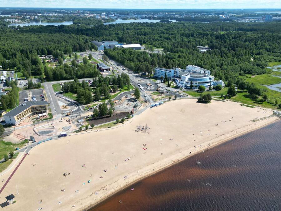 Vista aérea de una zona costera con playa arenosa, estacionamiento y una combinación de edificios residenciales y comerciales.