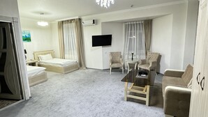 A spacious hotel room with a large bed, a sitting area with a sofa and armchairs, a television mounted on the wall, and a chandelier. - ALEXANDER HOTEL (Samarkand)