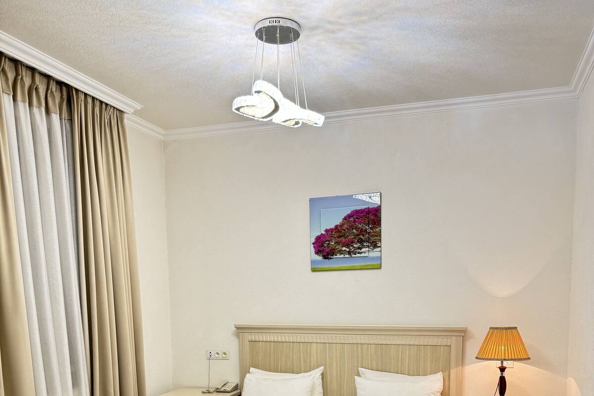 A hotel room with a bed, a nightstand, a lamp, a painting, and a window with curtains.
