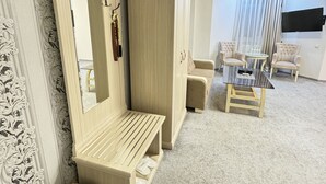A room with a large mirror, a bench, a wardrobe, a small table with chairs, and a television mounted on the wall. - ALEXANDER HOTEL (Samarkand)